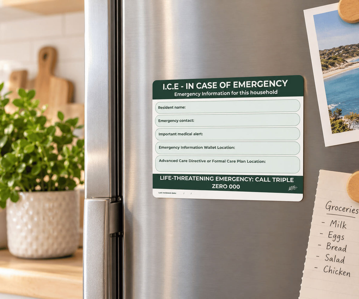 A rectangular emergency information card attached to a stainless steel refrigerator door in a kitchen setting. The card has a dark green header reading 'I.
